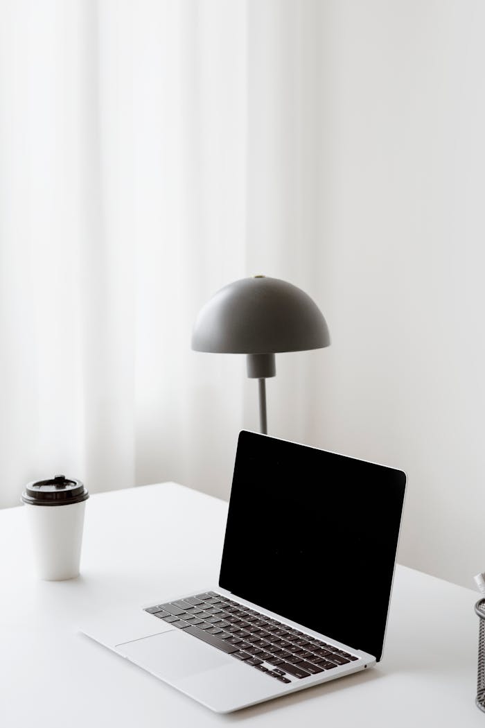 Clean workspace featuring a laptop, coffee cup, and modern lamp in a minimalist design.